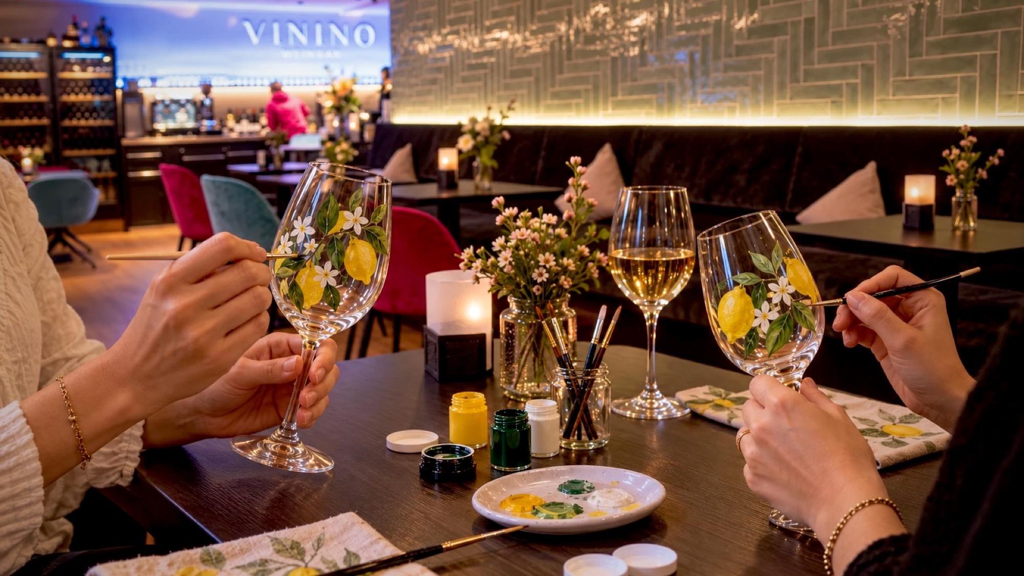 Zwei Gäste bemalen Weingläser mit Zitronen an einem Tisch im VININO
